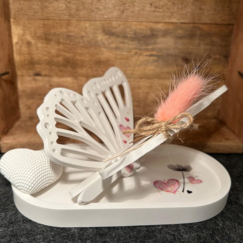 Handgefertigter märchenhafter Schmetterling aus Gießkeramik auf Sockel mit Herz- und Blumenmotiven, ergänzt durch Trockenblume und Herz aus Gießkeramik