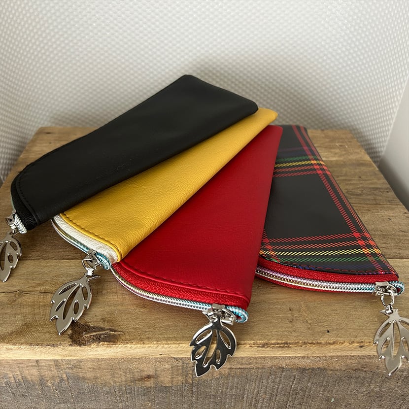 Vier handgemachte Brillenetuis aus Kunstleder – in Schwarz, Gelb, Rot und Karo-Design mit silbernem Blattanhänger