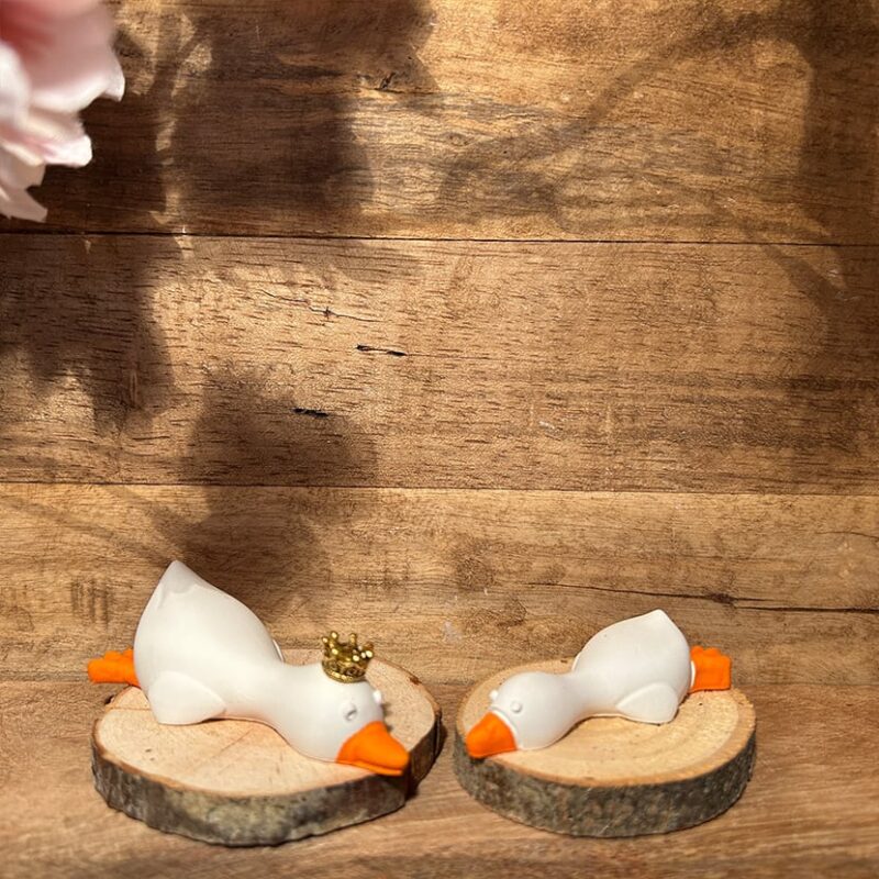 Zwei liegende Enten aus Gießkeramik, wahlweise naturweiß oder bemalt mit orangen Schnäbeln, Krone und Holzscheiben