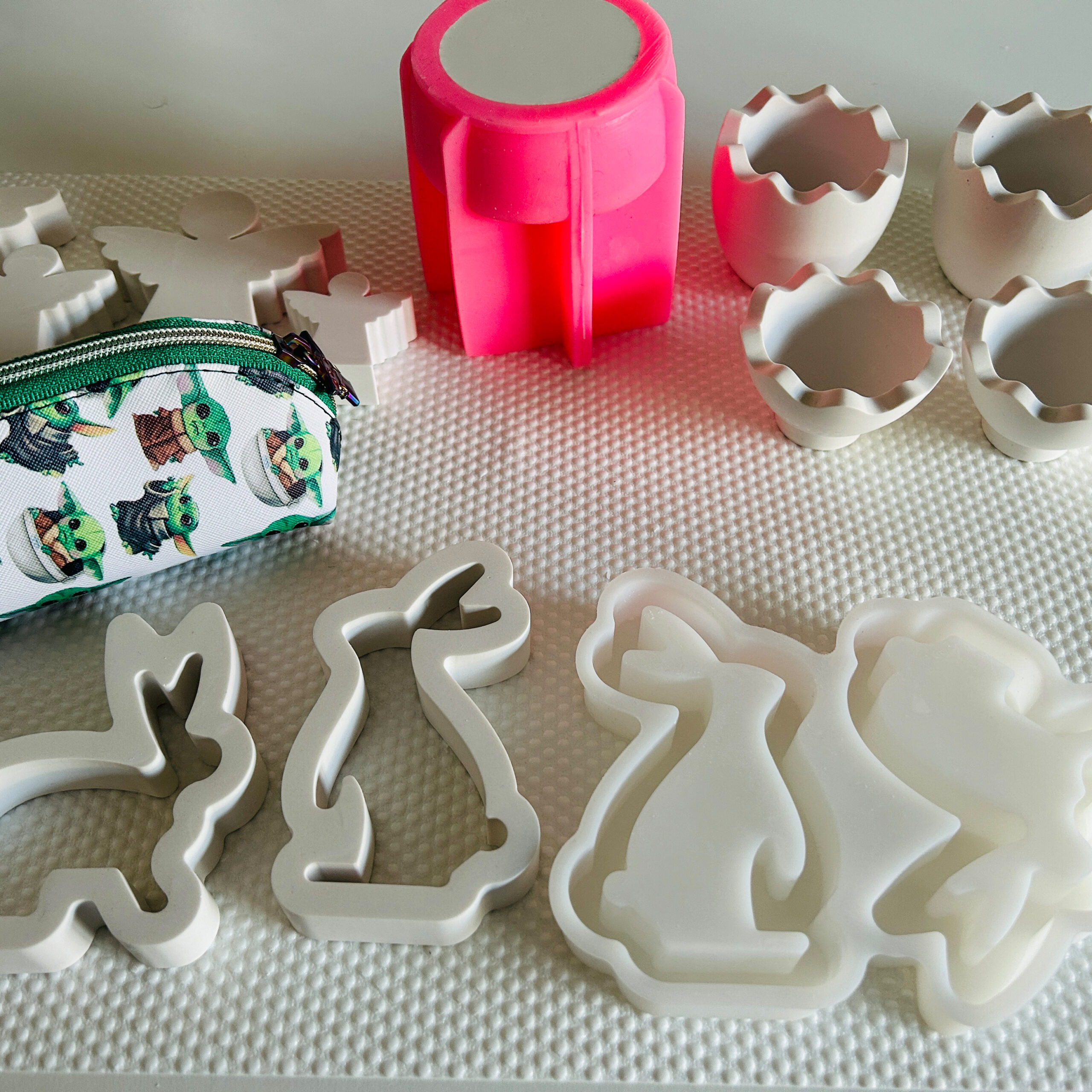 traum-stueck_tag-des-handwerks Silikonform, weiße Gießkeramik-Rohlinge in Tier- und Engel-Formen sowie Werkstattutensilien auf strukturierter Unterlage